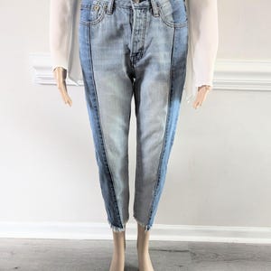 May include: A pair of blue denim jeans with a contrasting panel of lighter denim down the outside seam of each leg. The jeans have a frayed hem.