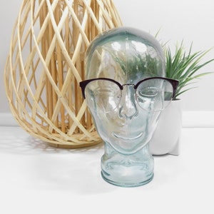 May include: A glass mannequin head with brown tortoiseshell glasses on a white background.