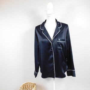 Peut inclure: Une chemise en satin noir avec des bordures blanches et un petit logo en forme de cœur blanc sur la poche poitrine.