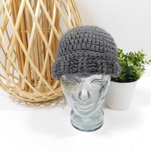 Puede incluir: Un gorro de punto de color gris sobre una cabeza de maniquí de vidrio. El gorro tiene una textura acanalada y un borde doblado.