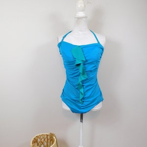 May include: A turquoise swimsuit with a green ruffle detail. The swimsuit has a halter neck style and is on a white mannequin.