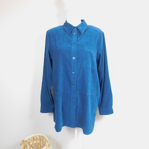 May include: A teal blue long-sleeved button-down shirt with a single pocket on the left chest. The shirt has a slightly oversized fit and features decorative stitching details.