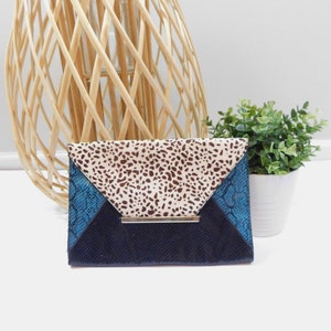 Könnte beinhalten: Eine blaue, schwarze und braune Clutch mit goldener Akzent. Die Clutch hat ein Leopardenmuster auf der oberen Klappe.