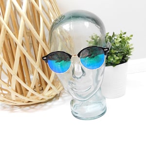 May include: Black framed round sunglasses with blue mirrored lenses on a glass mannequin head.
