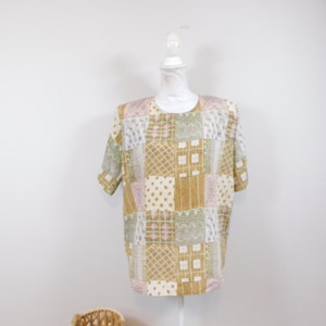 Pode incluir: Uma blusa de manga curta com um design de patchwork em tons de bege, verde e rosa. O tecido tem um aspeto texturizado e tecido.