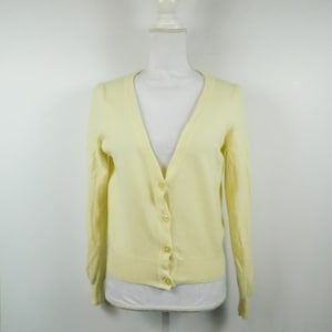 May include: A pale yellow cardigan with a v-neck and button closure. The cardigan has long sleeves and is made of a soft, knit fabric.