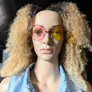 Könnte beinhalten: Eine Mannequin mit blonden Locken trägt runde, übergroße Sonnenbrillen mit einer rosa und einer gelben Linse.