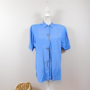 May include: A light blue short-sleeved button-down shirt with a silver chain and pearl accents.