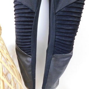 May include: Black leggings with faux leather panels on the knees. The leggings have a ribbed texture on the panels.