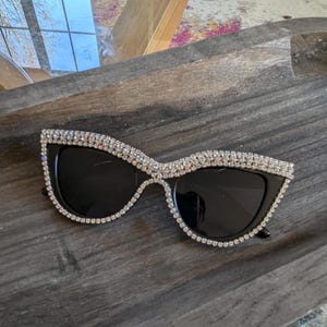 Puede incluir: Gafas de sol negras de ojo de gato con montura de strass. Las gafas tienen lentes negras.