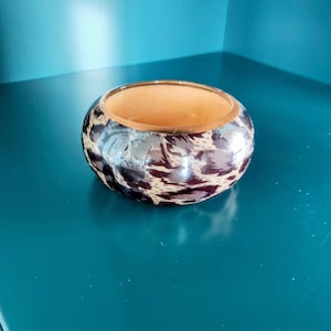 Puede incluir: Una pulsera tipo brazalete ancha con un llamativo estampado de leopardo en tonos marrón y negro en la superficie exterior. El interior de la pulsera circular es de un color tostado claro y liso, contrastando con el diseño animal.