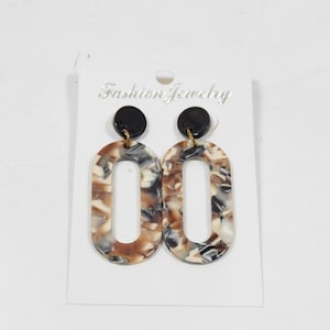 May include: A pair of brown, black and white oval-shaped earrings with a black and gold accent. The earrings are on a white card with the text "Fashion Jewelry".
