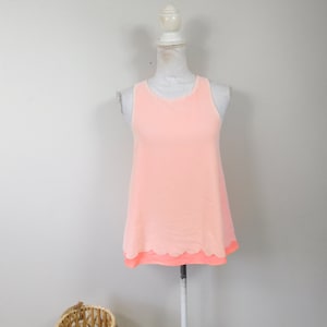 May include: A sleeveless peach-colored top with a scalloped hem. The top is on a white mannequin.