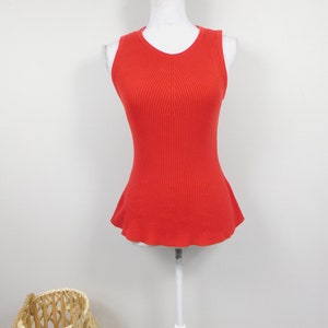 Pode incluir: Um top sem mangas de malha canelada em um tom vermelho vibrante. O top apresenta uma silhueta ajustada com uma bainha peplum flare. A peça é exibida em um manequim branco contra um fundo branco liso.