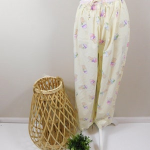 Może przedstawiać: Żółte spodnie do spania z wzorem lodów w różnych kolorach. Spodnie mają sznurek w pasie i są wykonane z miękkiej, wygodnej tkaniny.