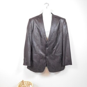 Peut inclure: Un blazer marron foncé avec une fermeture à deux boutons et des revers crantés. La veste est présentée sur un mannequin blanc sur fond blanc. Le blazer a deux poches avant et des poignets boutonnés.