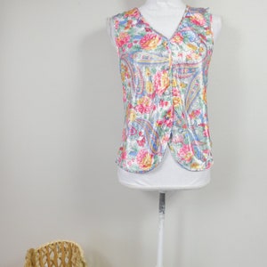 Puede incluir: Top sin mangas con estampado floral de cachemira en rosa, amarillo, azul y blanco. El top está abotonado en la parte delantera y se muestra en un maniquí blanco. La tela tiene un brillo sedoso.