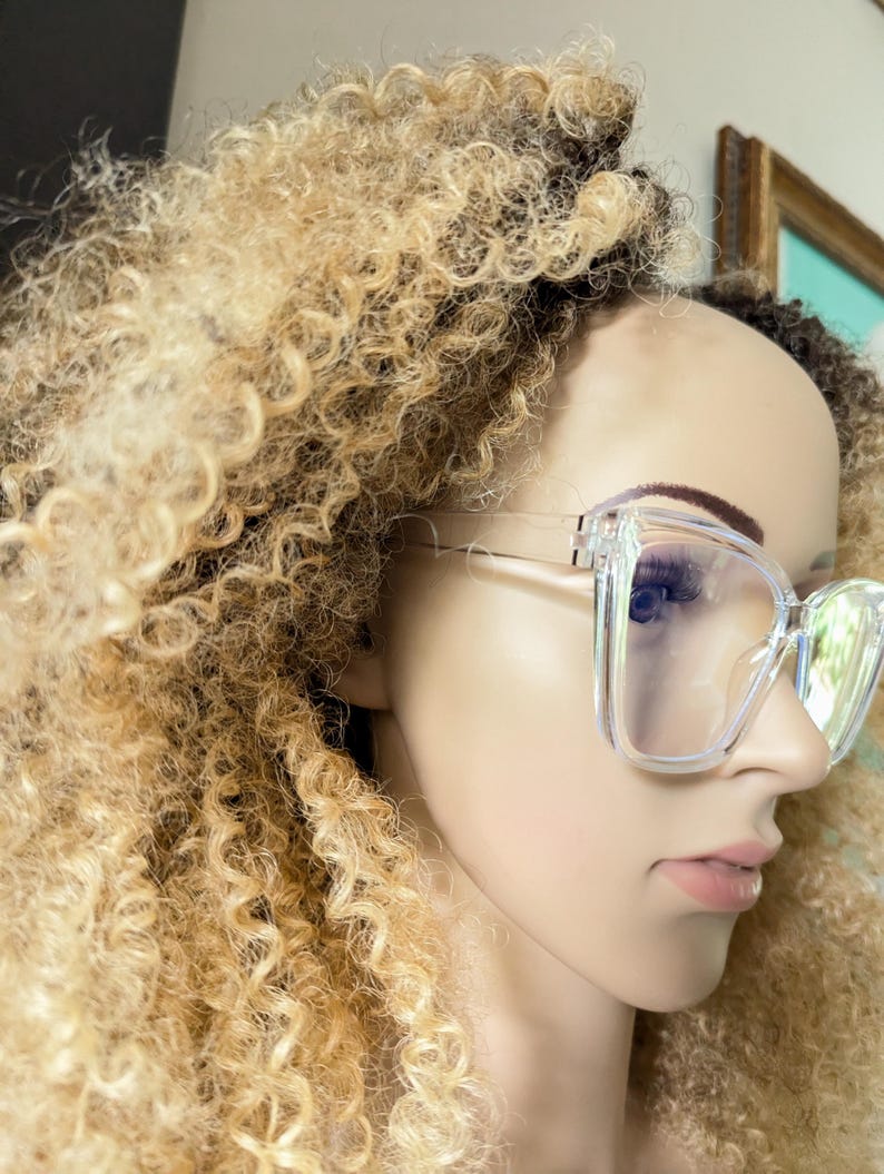 K&ouml;nnte beinhalten: Ein klarer Plastikrahmen mit quadratischen Gl&auml;sern. Die Brille sitzt auf einer Puppe mit blonden Locken.