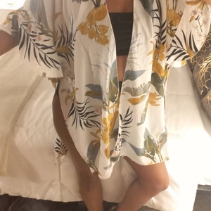 May include: White kimono with a tropical floral print in yellow, green, and gray. The lightweight, open-front garment features wide sleeves and a relaxed fit, perfect for layering over other clothing.