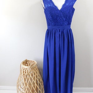 May include: A royal blue formal dress on a mannequin. The bodice features a V-neck and lace detailing, while the skirt flows to the floor. A woven lantern and potted plant are in the foreground.