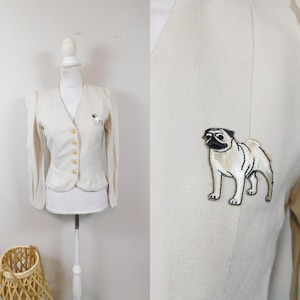 May include: A white blazer with a  pug embroidered on the front. The blazer has a v-neck and long sleeves.