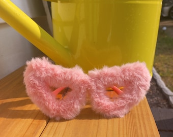 May include: Pink fuzzy heart-shaped sunglasses with a yellow background.