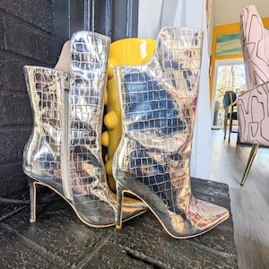 May include: A pair of silver metallic ankle boots with a pointed toe and stiletto heel. The boots have a crocodile-embossed pattern.