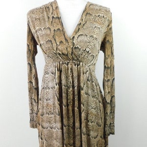 Könnte beinhalten: Langärmliges Kleid mit Schlangenmuster in Braun-, Beige- und Schwarztönen. Das Kleid hat einen V-Ausschnitt und eine geraffte Taille, die eine schmeichelhafte Silhouette erzeugt. Das Kleid wird auf einer weißen Schaufensterpuppe präsentiert.