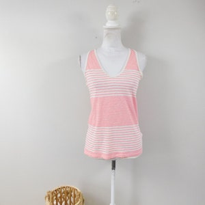 May include: A pink and white striped vest top with a V-neck is displayed on a white mannequin. The top has a classic striped pattern and a sleeveless design. A woven basket sits on the floor in front of the mannequin.
