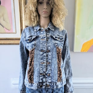 May include: A blue denim jacket with acid wash and leopard print panels. The jacket has a button closure and long sleeves.