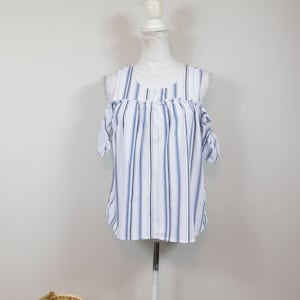 May include: A white and blue striped cold-shoulder top. The sleeveless blouse features vertical stripes in white, light blue, and navy blue. The top is displayed on a white mannequin. The top has a round neckline and short sleeves.