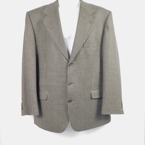 May include: A houndstooth blazer in shades of brown, tan, and gray. The jacket has a classic two-button closure, notched lapels, and two front pockets. The blazer is displayed on a white mannequin.
