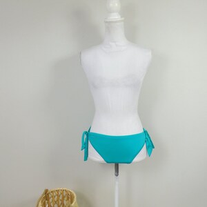 Könnte beinhalten: Türkiser Bikini-Unterteil mit Bindebändern an den Seiten auf einem weißen Mannequin.