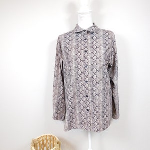 Op de afbeelding: Een lang mouw overhemd met knopen en een slangenhuidprint in bruine en witte tinten.