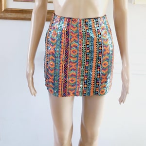 May include: A short, colourful, sequined skirt with a geometric pattern in shades of orange, blue, green, and pink.