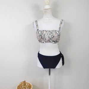 Può includere: Un costume da bagno a due pezzi con top a stampa di serpente e fondo nero tinta unita. Il top ha spalline sottili e scollo quadrato. Il fondo ha un laccio laterale.