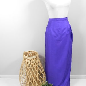 May include: A long purple skirt on a white dress form. The skirt has a simple design and a straight silhouette.