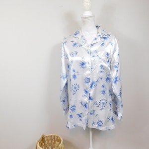 May include: A white satin shirt with a blue floral print. The shirt has a button-up front and long sleeves.