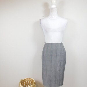 May include: A grey and white checked pencil skirt on a white mannequin. The skirt is knee-length and has a straight silhouette.