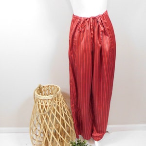 May include: Red and black striped satin pants with a drawstring waist. The pants are on a white mannequin.