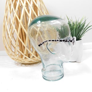 May include: A clear glass mannequin head with a black and white patterned eyeglass frame resting on the nose. The mannequin head is sitting on a white surface.