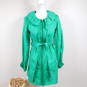 Könnte beinhalten: Eine langärmelige Jacke in leuchtendem Grün mit einem Rüschenkragen und einem Reißverschluss. Die Jacke hat einen Gürtel und einen leicht ausgestellten Rock.