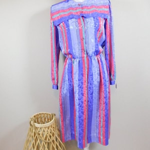 May include: A long-sleeved dress with a pink, blue, and white striped pattern. The dress has a ruffled collar and a button-up front.