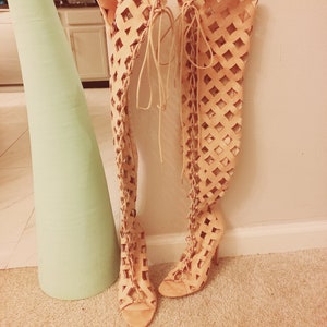 May include: A pair of beige thigh-high boots with a lace-up design and open toe.