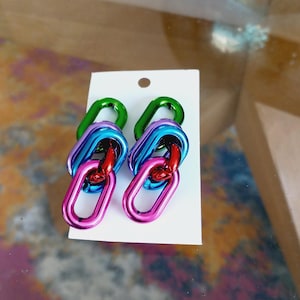 May include: A pair of colorful earrings with three linked oval shapes. The earrings are made of metal and are in shades of green, blue, red, and pink.
