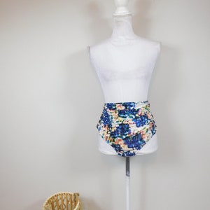 Könnte beinhalten: Hoch sitzende Badehose mit einem bunten abstrakten Muster auf weißem Hintergrund. Der Badeanzug befindet sich auf einem weißen Mannequin.
