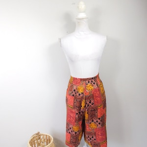 May include: Red, orange, and black patterned shorts with a high waist and elastic waistband. The shorts are on a white mannequin.