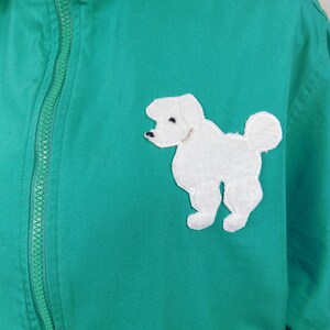 May include: A green zip-up jacket with a white embroidered poodle on the right side.
