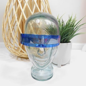Könnte beinhalten: Ein blaues Plastikvisier mit einer geschwungenen Form. Das Visier befindet sich auf einem Glas-Mannequin-Kopf.