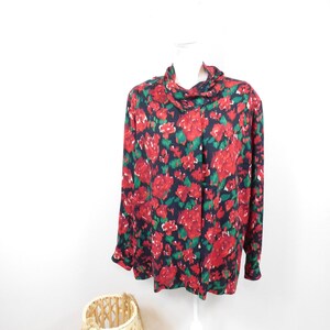 May include: A long-sleeved, black blouse with a red and green floral print. The blouse has a high neck and a relaxed fit.